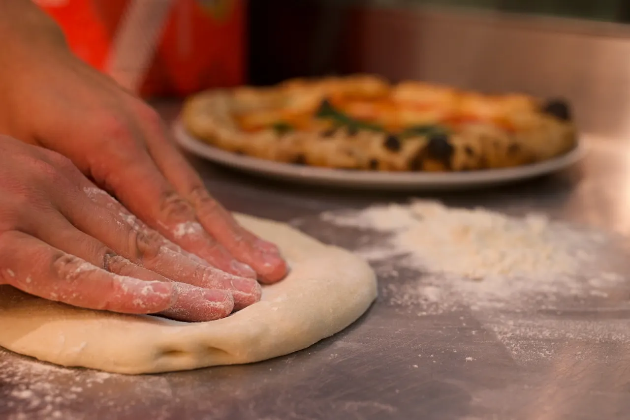 Pressing a dough ball flat from the centre, leaving the rim